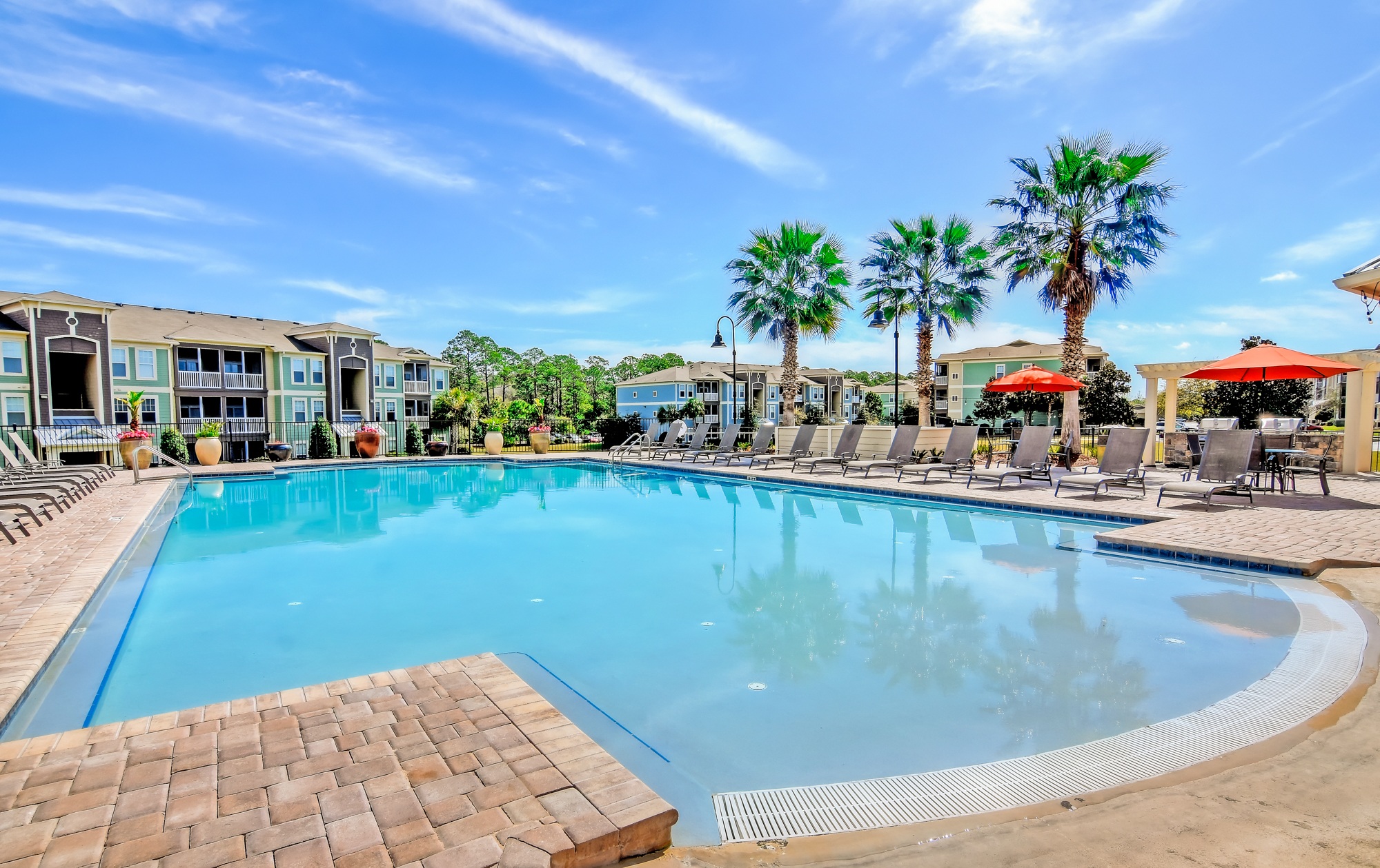 A large outdoor swimming pool surrounded by palm trees and lounge chairs.